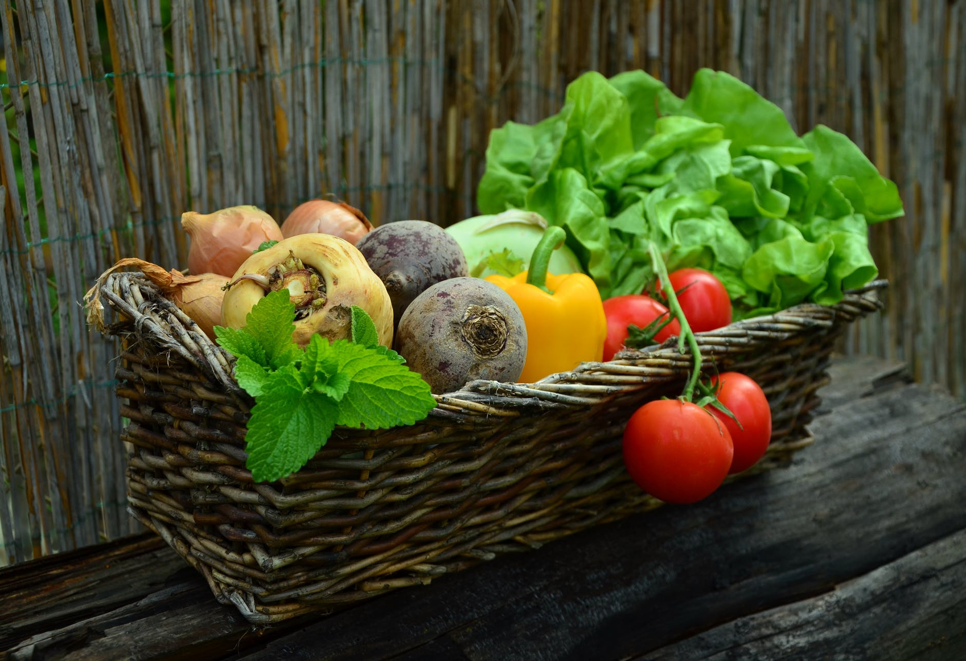 red tomato besides green vegetable leaf on brown basket