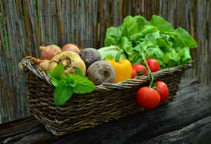 red tomato besides green vegetable leaf on brown basket